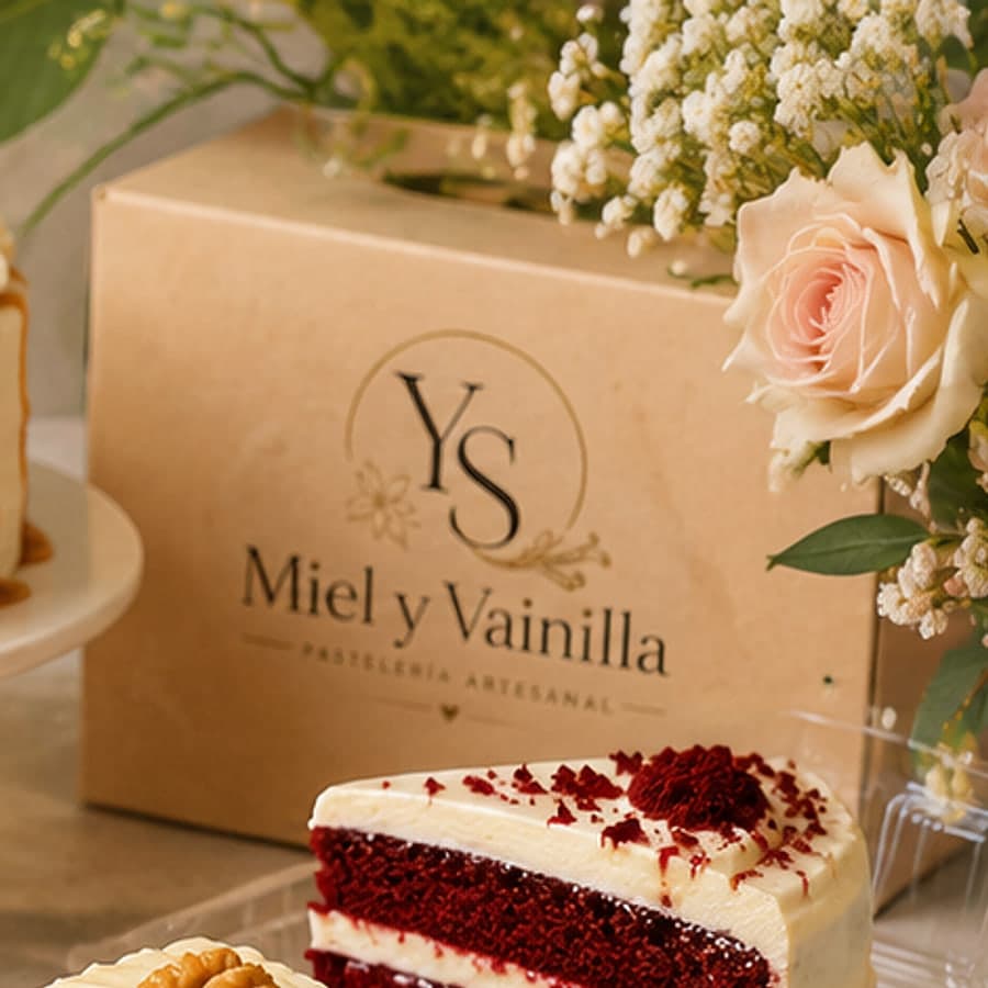 Caja de regalo de Miel y Vainilla con el monograma YS, acompañada de una porción de torta y un arreglo floral