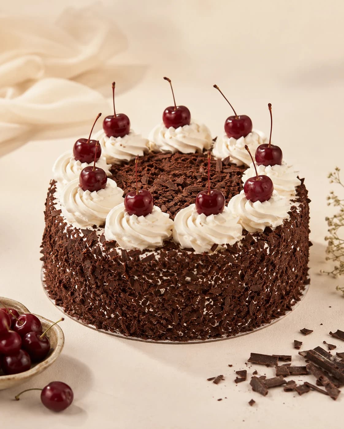 Torta Selva Negra cubierta de viruta de chocolate, con rosetones de crema chantilly y cerezas con tallo
